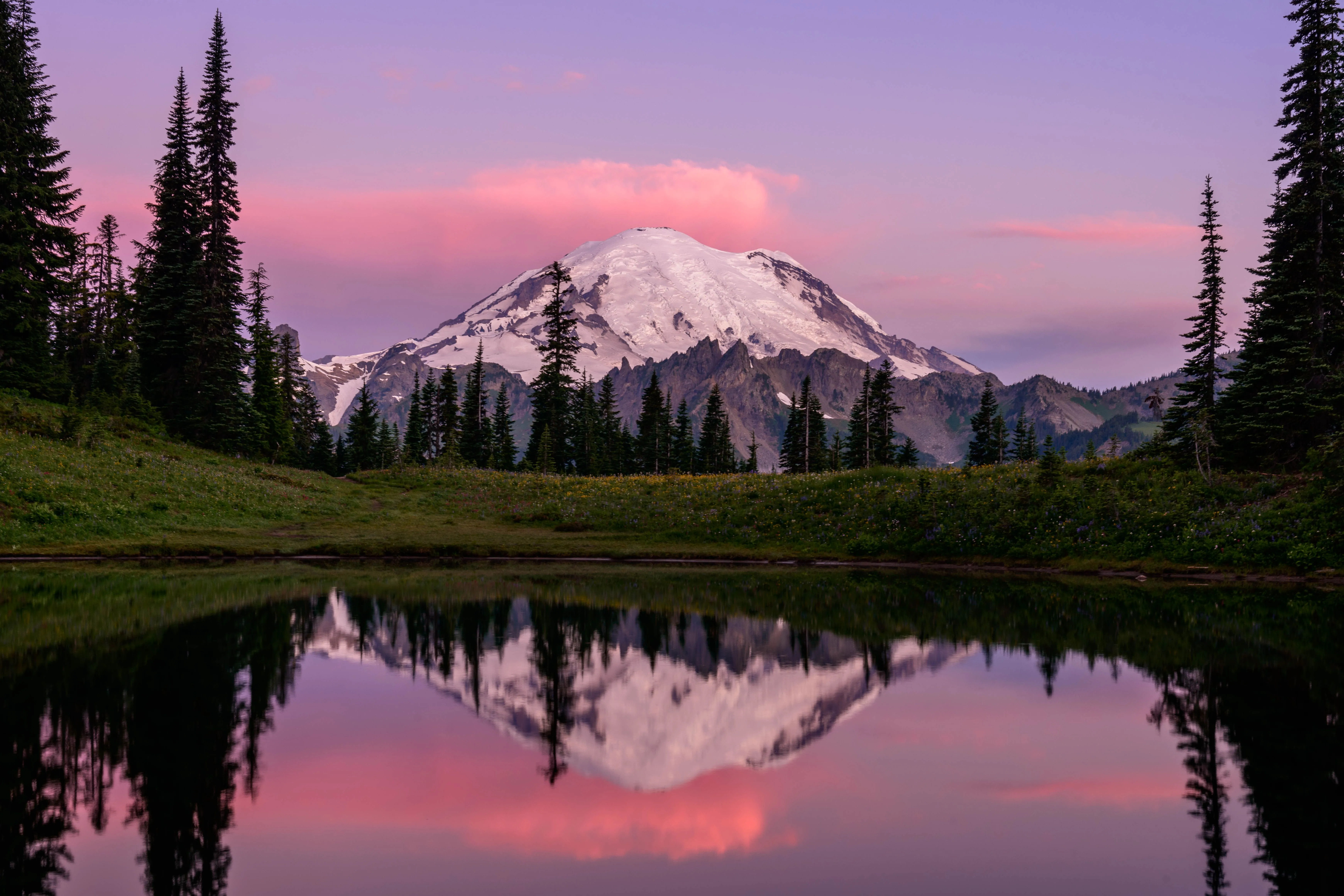 Mount Rainier at dusk, its snowcap lit pink and reflected in a still alpine lake